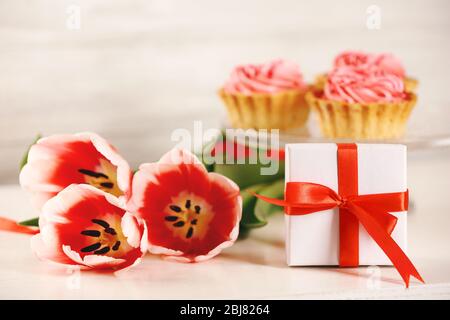 Geschenk-Box mit Tulpen und Cupcakes auf verschwommenem Hintergrund Stockfoto