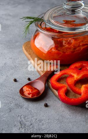 Ajvar in einem Glasgefäß auf grauem Hintergrund. Nahaufnahme Stockfoto