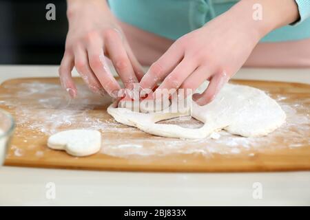 Junge Frau, die die Herzen in einem Teig auf der Küchentheke ausschneidet Stockfoto