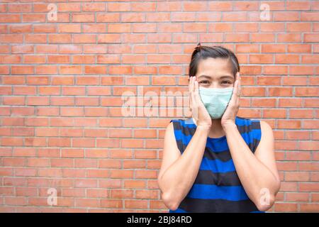 Die Hand, die die Maske auf asiatische Frau Gesicht Backstein Wand. Stockfoto