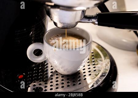 Nahaufnahme des italienischen schwarzen Kaffees, der morgens aus einer Kaffeemaschine in eine Cappuccino-Tasse tropft Stockfoto