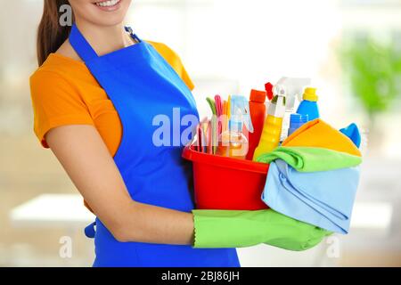 Frau in Gummihandschuhen hält Waschbecken mit Waschmitteln auf verschwommenem Hintergrund Stockfoto