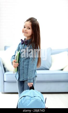 Kleines Mädchen mit blauer Rückenverpackung, die Notizbücher im Wohnzimmer hält Stockfoto