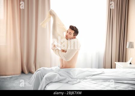 Junger Mann, der im Bett aufwacht und sich kleidet. Stockfoto