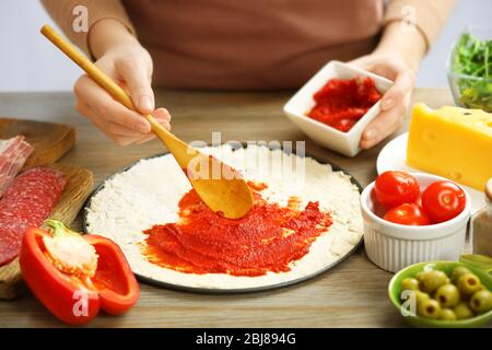 Frau, die eine Pizza auf einem Holztisch macht, Nahaufnahme Stockfoto