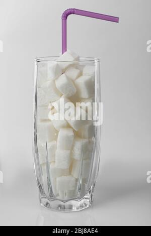 Longdrinkglas mit Klumpenzucker und Cocktailstroh auf grauem Hintergrund Stockfoto