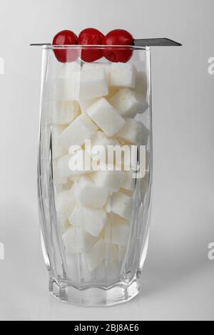 Longdrinkglas mit Klumpenzucker und Cocktailkirschen auf grauem Hintergrund Stockfoto