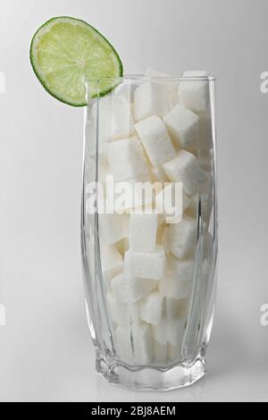 Longdrinkglas mit Klumpenzucker und Limettenscheibe auf grauem Hintergrund Stockfoto