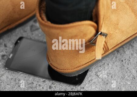 Weibliche Stiefel zerquetschen ein Handy auf dem Bürgersteig Stockfoto