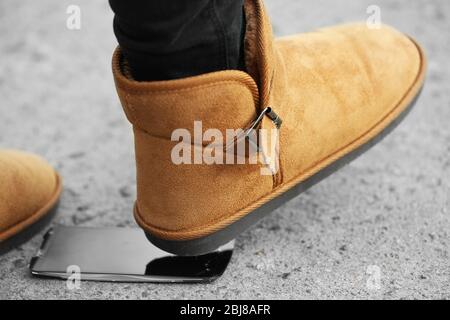 Weibliche Stiefel zerquetschen ein Handy auf dem Bürgersteig Stockfoto