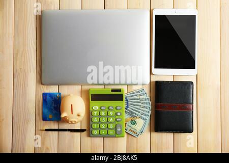 Sparschwein mit Laptop, Tablet, Geld und anderem Zubehör auf Holztisch, Draufsicht Stockfoto