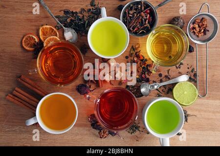 Tassen mit verschiedenen Teesorten und Zutaten auf dem Tisch Stockfoto