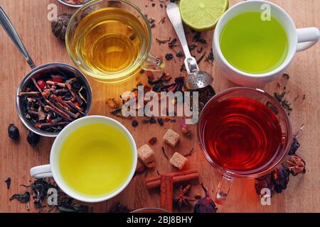 Tassen mit verschiedenen Teesorten und Zutaten auf dem Tisch Stockfoto