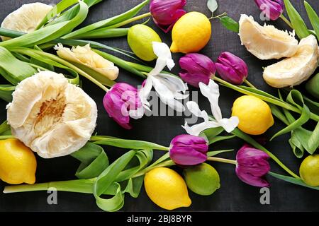 Frische violette Tulpen, Iris und Zitrusfrüchte auf schwarzem Hintergrund, Draufsicht Stockfoto