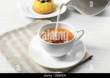 Milch in eine Tasse Tee gegossen, Nahaufnahme Stockfoto