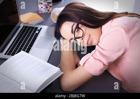 Junge Frau schlief ein, während sie Laptop am Tisch benutzte Stockfoto