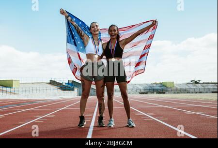 Zwei Läuferinnen feiern auf der Strecke mit amerikanischer Flagge. Siegerathlet mit der US-Flagge im Stadion. Stockfoto