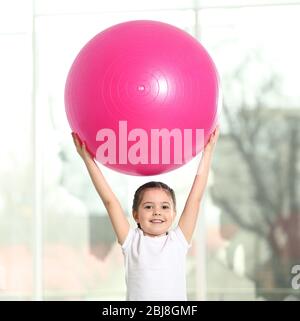 Kleine süße Mädchen tun Übungen mit Ball drinnen Stockfoto