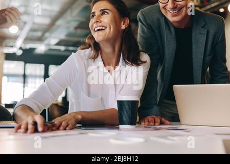 Lächelnde Geschäftsfrau, die während eines Meetings am Tisch sitzt und mit Kollegen spricht. Geschäftsleute, die während des Meetings zwangloses Gespräch führen. Stockfoto