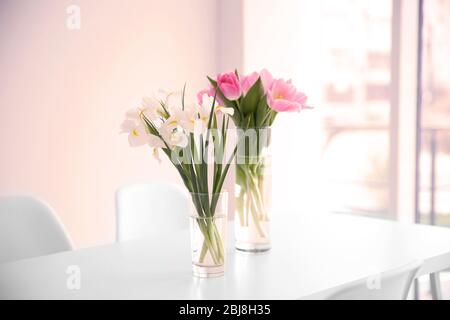 Schöne Tulpen und Iris auf Esstisch vor weißem Hintergrund Wand Stockfoto