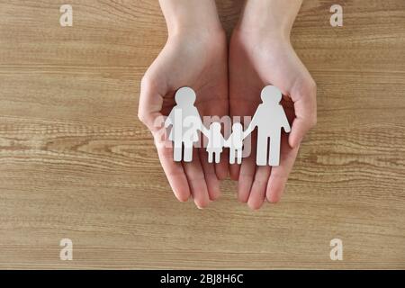 Weibliche Hände halten Familienfigur auf Holzhintergrund Stockfoto