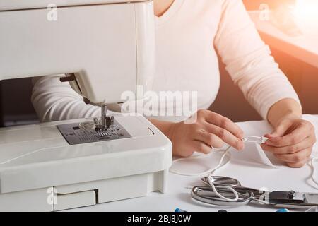 Frauenhände in weißer Kleidung nähen neben der Nähmaschine. Gesichtslos. Copyspace. Stockfoto