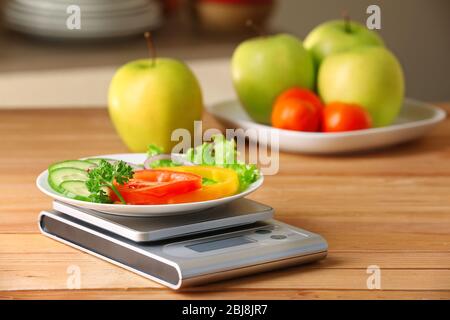 Teller mit frischem Gemüse und digitale Küchenwaagen auf Holztisch Stockfoto