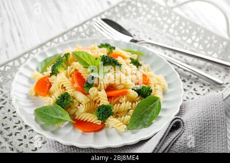 Gekochte Fusilli-Pasta mit Karotte, Brokkoli und Basilikum auf weißem Teller Stockfoto