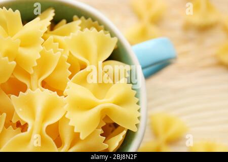 Trockene Farfalle Pasta in blauer Tasse auf Holztisch Stockfoto