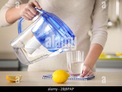 Frau gießt Wasser aus der Filterkanne in Glas in der Küche Stockfoto