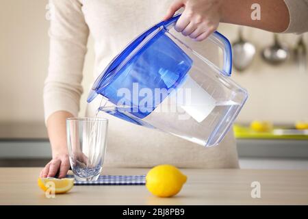 Frau gießt Wasser aus der Filterkanne in Glas in der Küche Stockfoto