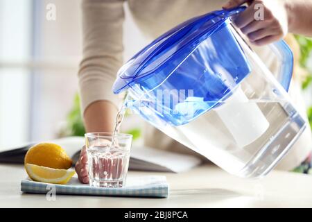 Frau gießt Wasser aus der Filterkanne in Glas in der Küche Stockfoto