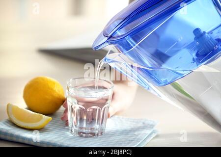 Wasser aus der Filterkanne in das Glas in der Küche gießen Stockfoto