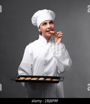Professioneller Koch verkostet Plätzchen von einem Tablett auf grauem Hintergrund. Stockfoto