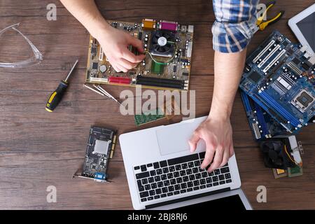 Männliche Hände Reparatur Computer-Details und mit Laptop auf Holztisch, Draufsicht Stockfoto