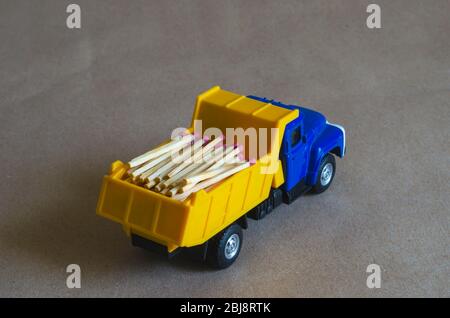 Ein gelber Kipper mit einem blauen Fahrerhaus trägt Streichhölzer. Spielzeugwagen mit einem ganzen Körper aus Holz Streichhölzer. Kreativer industrieller Hintergrund. Protokollierung und Logisti Stockfoto