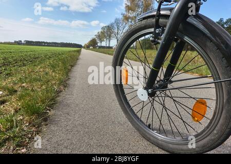 Vorderrad eines Fahrrads auf einem gepflasterten Radweg, der neben einer Reihe von Bäumen in der Ferne verschwindet, Konzeptfoto für Fahrradtour Stockfoto