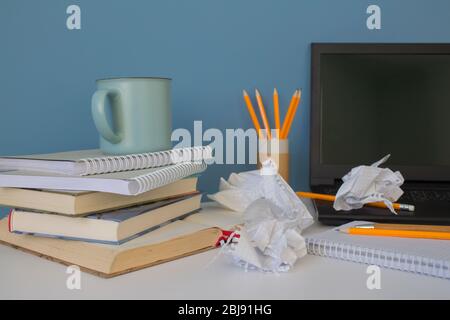 Vorderansicht auf Chaos oder Chaos auf weißem Tisch mit schwarzem Laptop, Büchern, Tasse Kaffee und gelben Bleistiften auf wiederverwendbarem Papierrohr. Home Office von kreativen Stockfoto