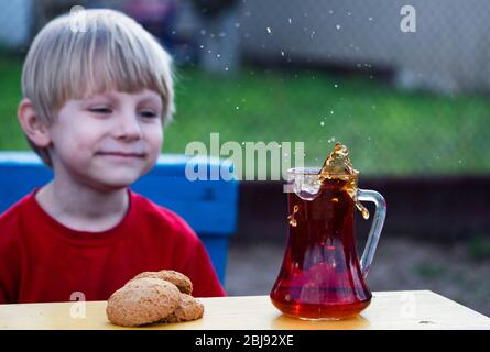 Kaukasischer Junge beobachtet einen Spritzer Tee in einer Tasse von einem fallenden Stück Zucker Stockfoto