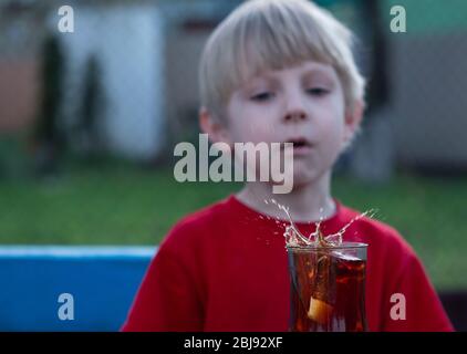 Kaukasischer Junge beobachtet einen Spritzer Tee in einer Tasse von einem fallenden Stück Zucker Stockfoto