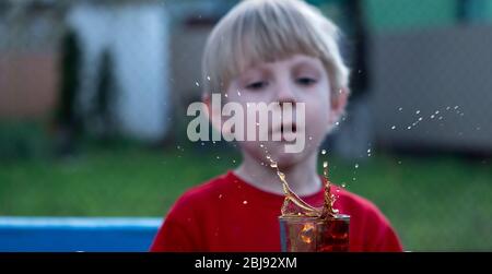 Kaukasischer Junge beobachtet einen Spritzer Tee in einer Tasse von einem fallenden Stück Zucker Stockfoto