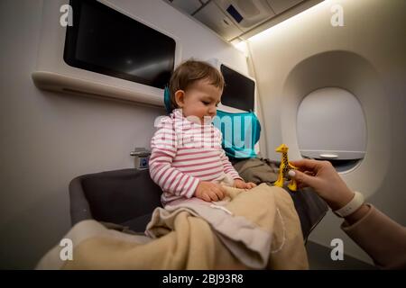 Mama Hand spielt ein Spielzeug mit einem glücklichen lächelnden kleinen niedlichen Kleinkind sitzt in der Babybinde eines Flugzeugs. Close-up, weiche Fokus. Stockfoto