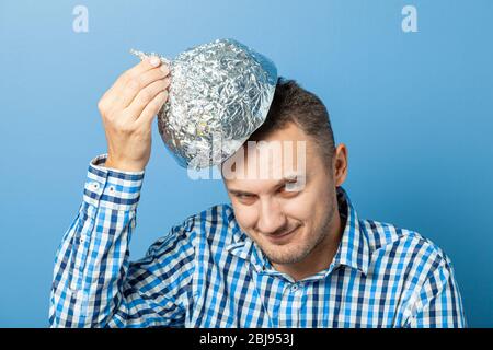 Mann setzt auf einen Helm aus Aluminiumfolie mit zufrieden Gesicht.. Schützt vor dem Lesen denken. Stockfoto