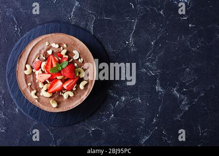 Pflanzenbasiert, nicht backen vegane Dessert Schokolade Käsekuchen mit No-Bake Kruste aus Datteln, Kakao und Pekannüsse mit Erdbeeren und Minze auf einem dunklen con Stockfoto