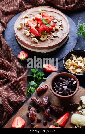 Festliche dreifache Schokoladenkuchen mit eingeweichten Cashewnüssen Mousse Füllung und No-Bake Datteln, Kakao und Pekannüsse, dekoriert mit frischen Erdbeeren auf der Oberseite, Stockfoto