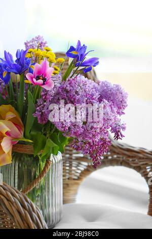 Bouquet von frischen Frühlingsblumen auf Korbstuhl drinnen Stockfoto