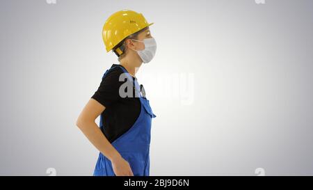 Bauarbeiterin in Overalls und in medizinischer Maske auf Steigungshintergrund. Stockfoto