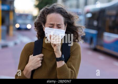 Kaukasische Frau mit einer Schutzmaske und hustet auf den Straßen Stockfoto