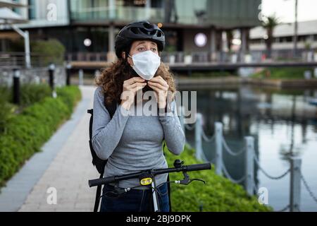 Kaukasische Frau, die eine Schutzmaske aufsetzt und einen Fahrradhelm auf den Straßen trägt Stockfoto