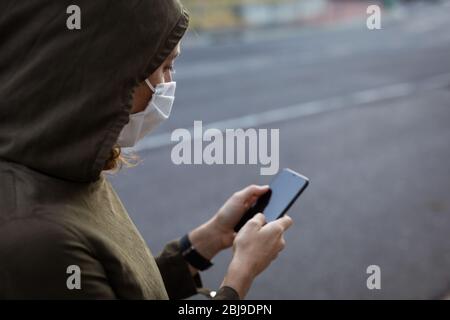 Kaukasische Frau, die eine Schutzmaske trägt und ihr Telefon auf der Straße benutzt Stockfoto